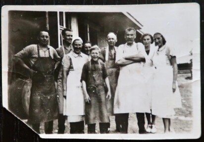 Män, kvinnor och barn i arbetskläder uppställda för foto iförda vita och svarta förkläden.