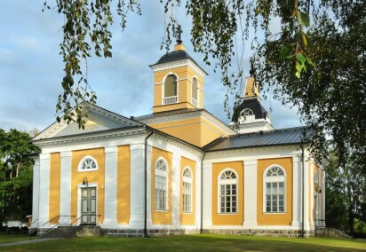 Malax kyrka i gult och vitt och byggd i ett kors. En klockstapel syns i bakgrunden.